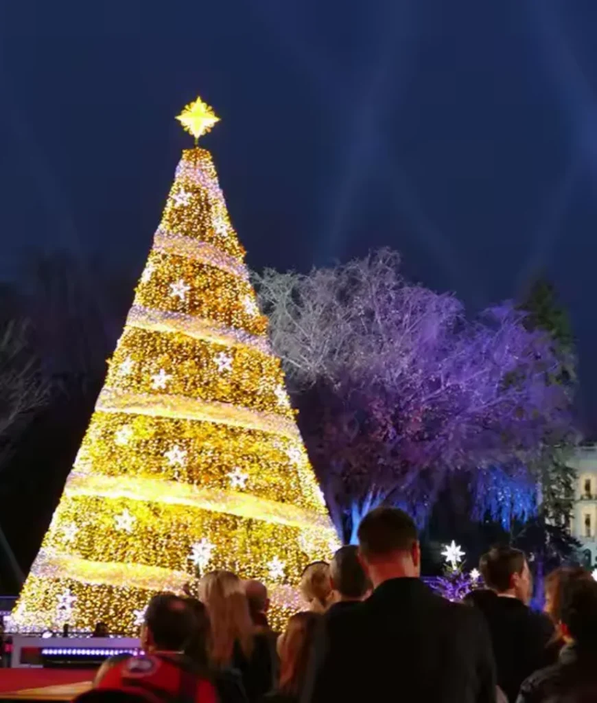 A massive golden Christmas tree with twinkling stars, surrounded by a crowd.