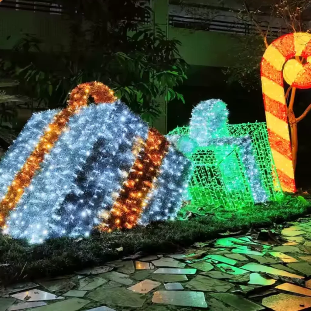 Oversized glowing Christmas presents in blue, green, and gold lights, arranged in a festive outdoor setting.